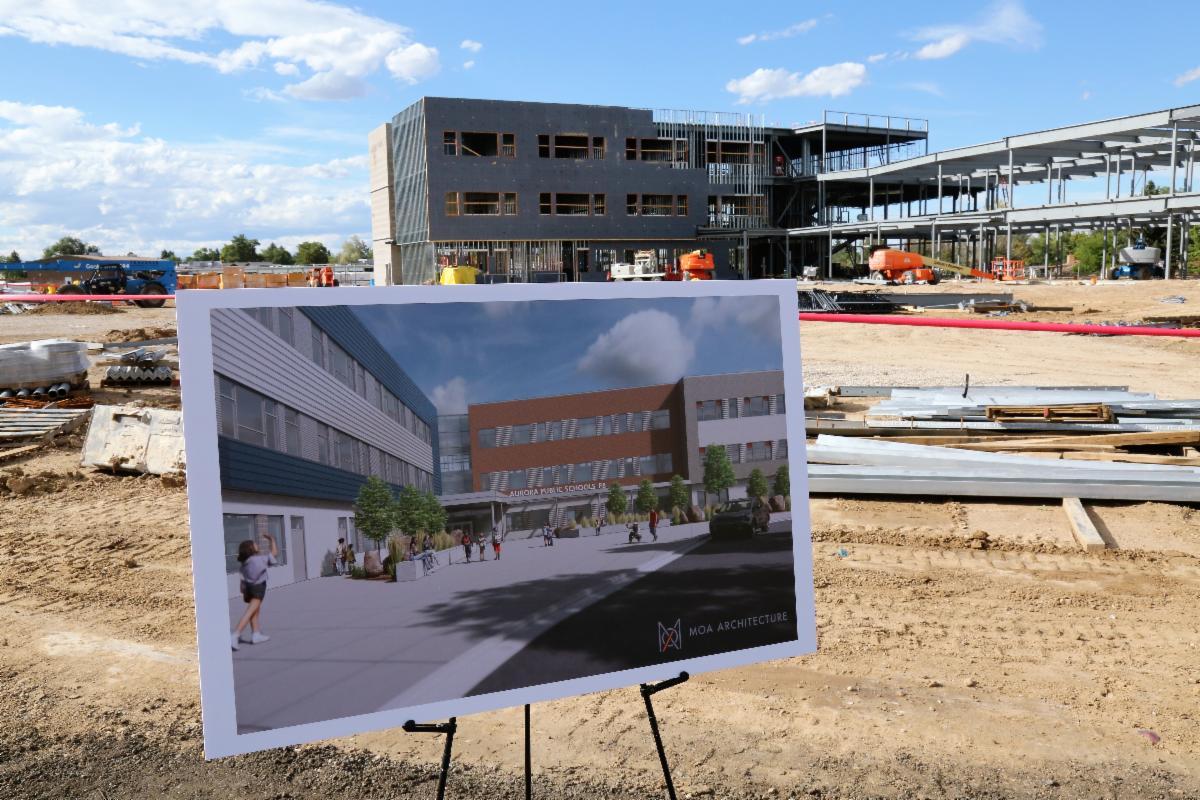 an APS school being built with a drawing of the building set up on a stand in front of it