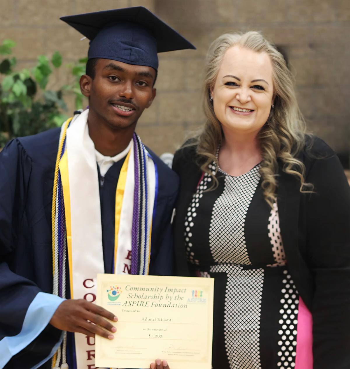 staff member with a student graduate holding up a scholarship