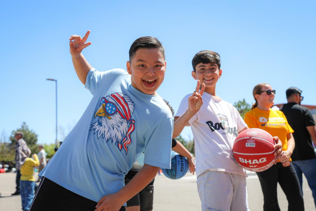 Two smiling elementary students giving two thumbs up and one student is holding a basketball.
