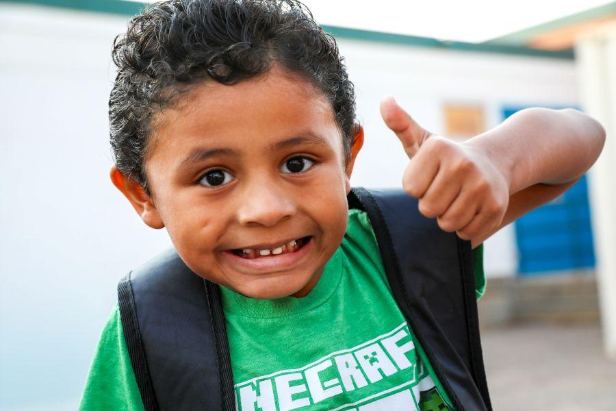 A smiling elementary school student gives a thumbs up.