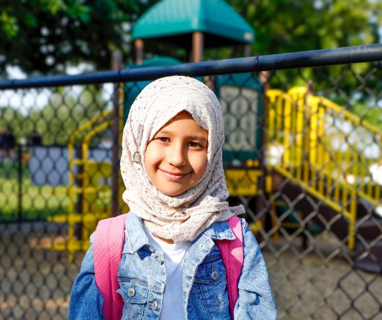 Smiling elementary school student standing in front of a fence and playground