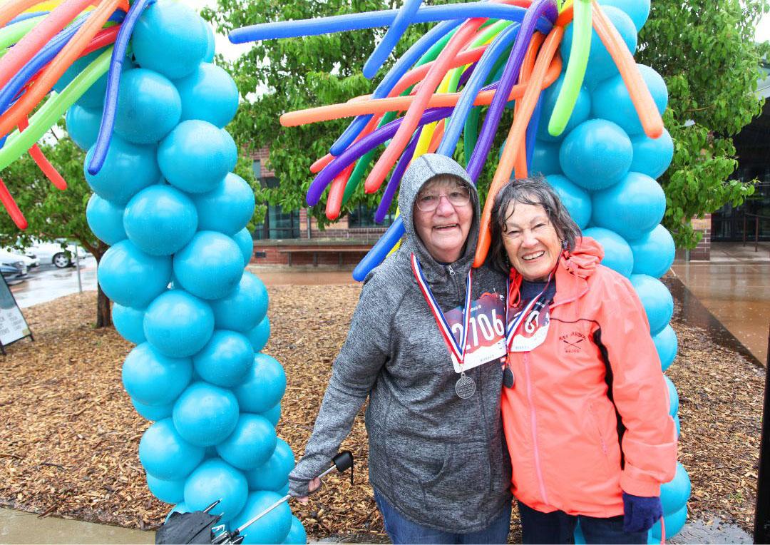 Two active adults stand in front of balloon structures at the Aurora Center for Active Adults Walk and Roll event