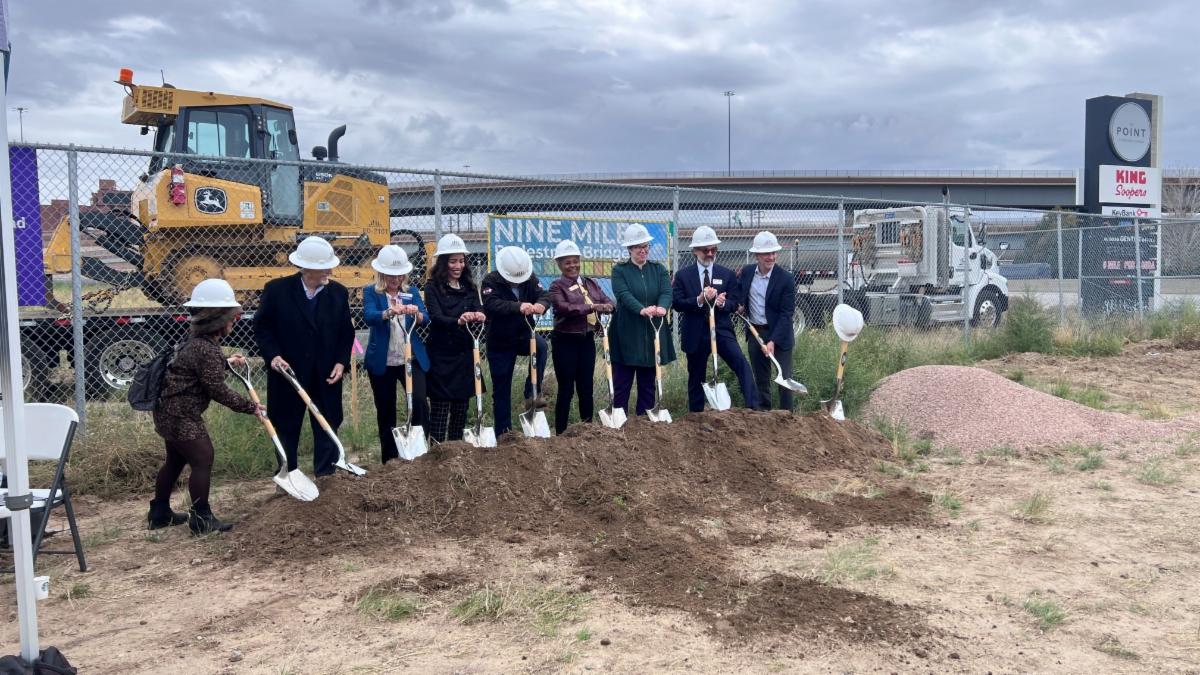 This image of people lined up with shovels at a dirt pile with construction equipment behind them links to the Nine Mile Pedestrian Bridge webpage