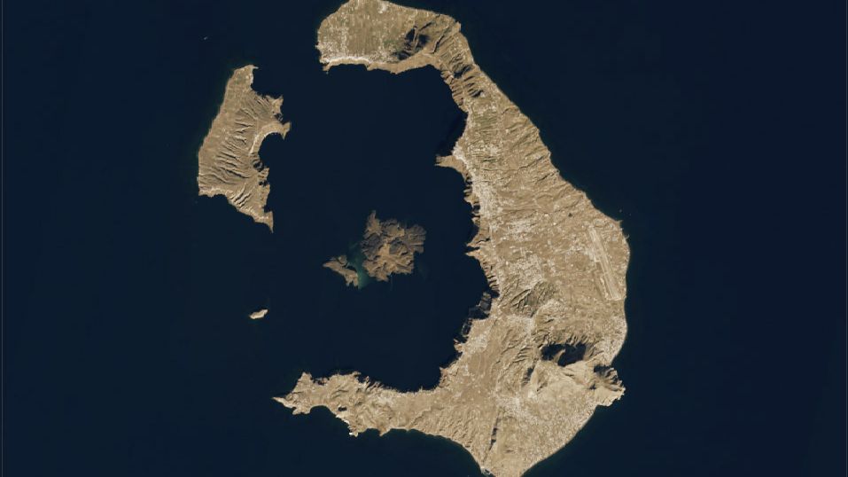 A satellite image shows the horseshoe-shaped island of Santorini set within the blue expanse of the Aegean Sea along with three smaller neighboring islands to the west.