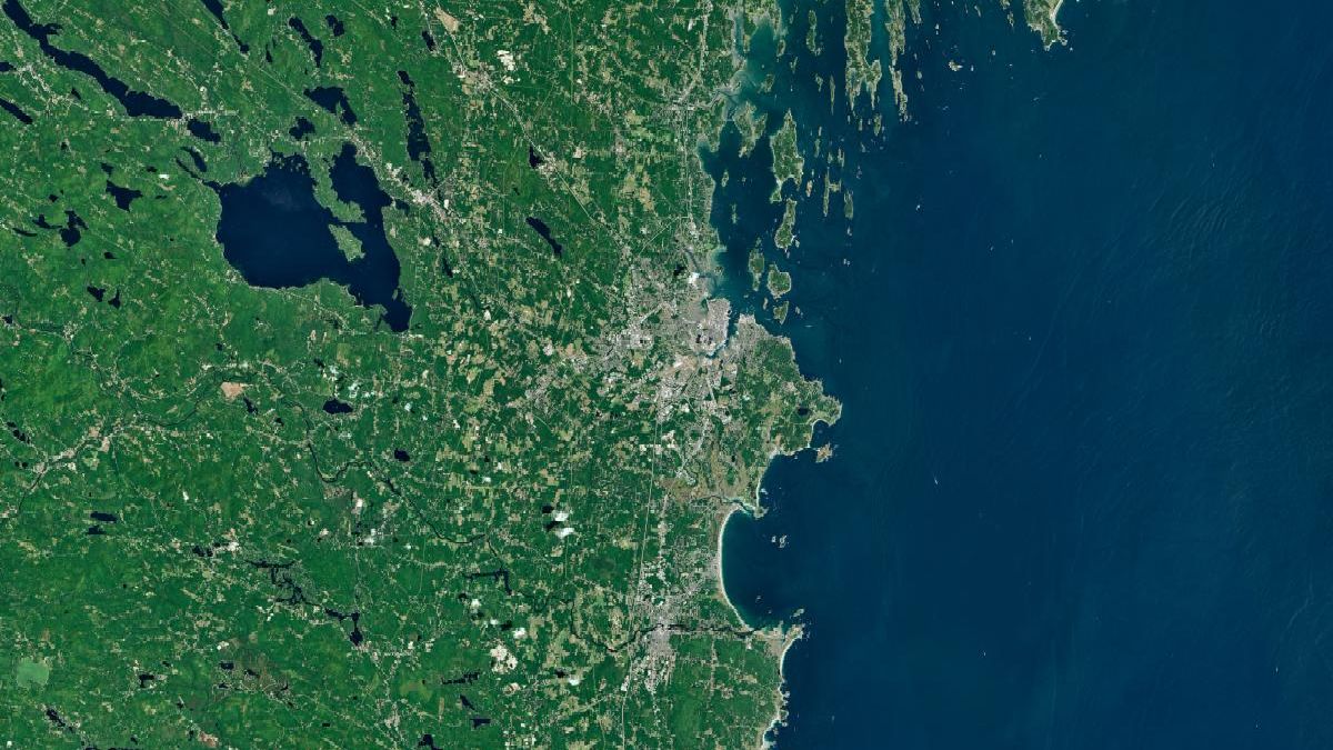 A satellite image of the Maine coastline highlights smooth, sandy beaches near Saco Bay on the left and the rocky, jagged coastal features near Casco Bay on the right.
