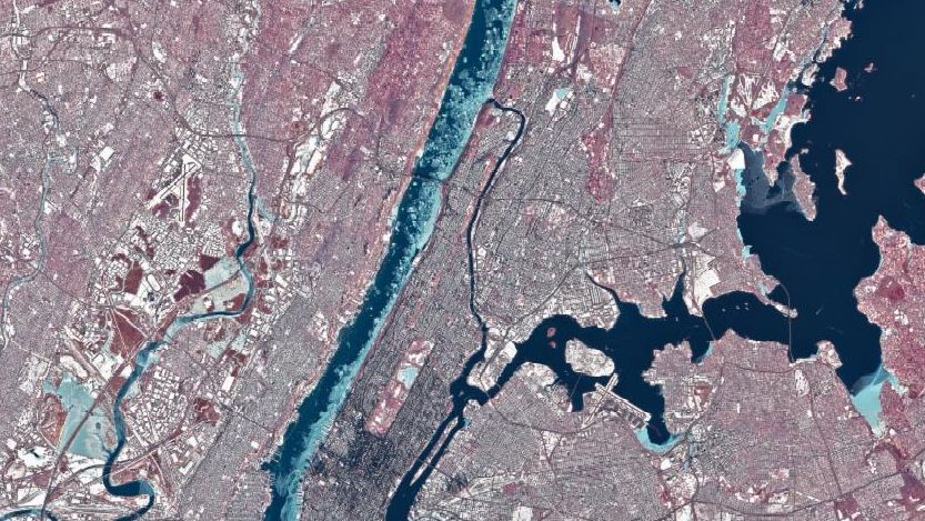 Chunks of ice, which appear light blue in this false-color image, line the western shore of Manhattan in the Hudson River. Smaller rivers and lakes in the scene also appear frozen or partially frozen. The ground is snow-covered, and tall buildings cast long, dark shadows.