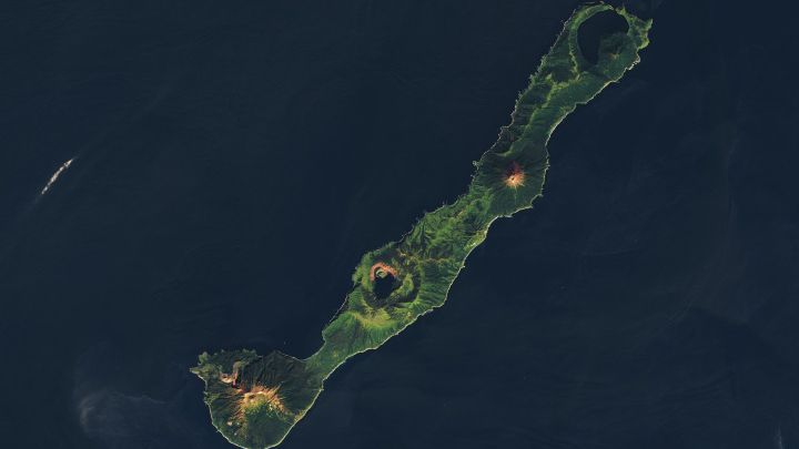 A natural-color Landsat 8 satellite image of an island in the Kuril Archipelago between northern Japan and Russia. This light and dark green island appears like the letter I tilted at 45 degrees, with circular bumps along the land where volcanoes and caldera’s sit. This image also features text to pinpoint locations such as the Sea of Okhotsk, Simushir Island, Zavaritskogo Caldera, and the Pacific Ocean. This image was acquired on September 12, 2024. 