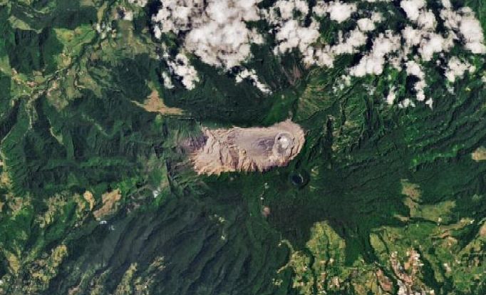 The summit area of Volcán Poás (Poás volcano) occupies the center of a detailed satellite image. An elongated area oriented horizontally appears tan with no vegetation; a round crater is located in the right portion of this area. Rugged-looking light and dark green mountain slopes take up the rest of the image, and some clouds are present across the top edge.