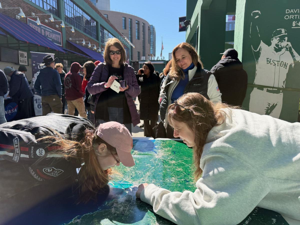 People stand around a table with a Landsat image of the Boston area. 