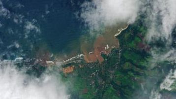 The same area, with brown floodwater pooling across farmland between Mokuleia and Waialua, with a red-brown plume spreading into the coastal ocean.