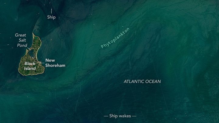 Natural-color Landsat 8 image of Block Island in the Atlantic Ocean, acquired on July 3, 2024. The island itself is pear-shaped. A combination of sunglint and a phytoplankton bloom made the wakes trailing behind the many boats near the island especially visible at the time of this image. White text labels Block Island, New Shoreham, Great Salt Pond, Ship, Ship wakes, Phytoplankton, and the Atlantic Ocean.