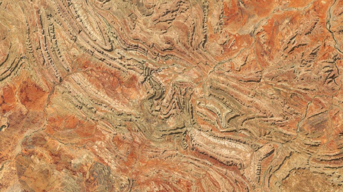 A satellite image shows several curving ridges that are part of the Davenport Range in a desert landscape in northern Australia. Near the center of the image, the mostly parallel ridges become jumbled and cut abruptly toward the southeast. Geologists have assembled evidenced showing that the deformation was caused by an asteroid collision about 600 million years ago.