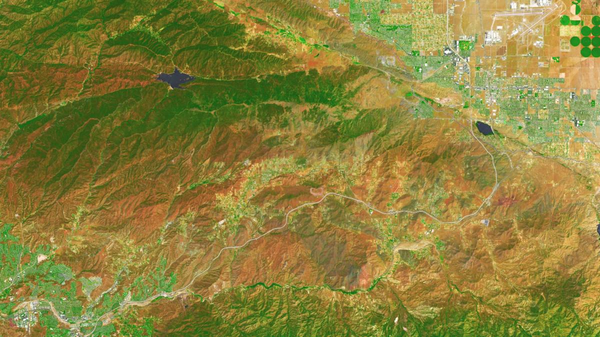 In this false-color image, areas with more extensive vegetation on the Sierra Pelona retain more moisture than the hills surrounding Agua Dulce, making the Sierra Pelona appear dark green in comparison to the rusty brown coloration of the lower hills. Vasquez Rocks appears as a patch of curved gray stripes near the center of the image.