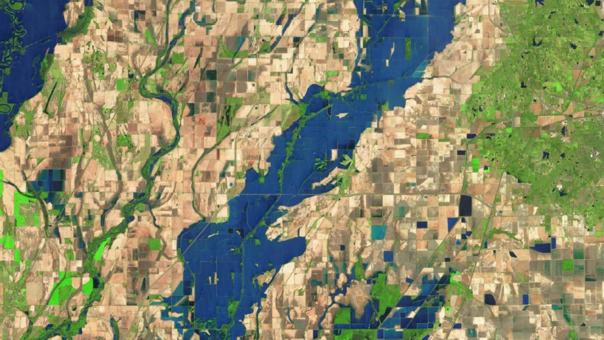A more recent false-color satellite image shows the same area on April 15, 2025. Now, floodwaters from the Cache River spill across farmland along the banks of the river. Water appears blue and vegetation is green.
