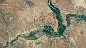 The reservoir is nearly empty by May 2026. The Gila River's natural channel is now visible and flanked with green vegetation in what had been the bottom of the reservoir.