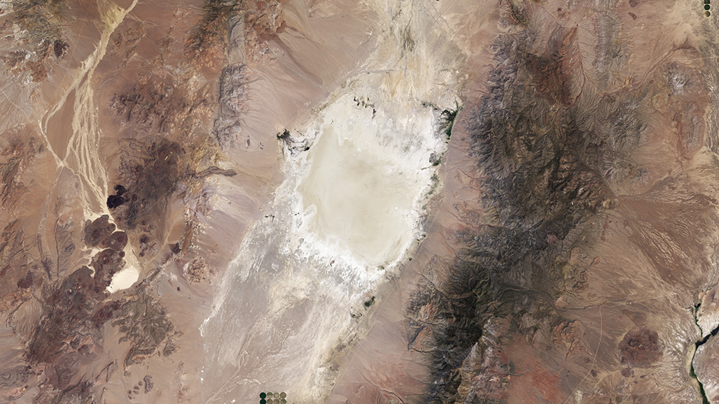 A Landsat image of Railroad Valley Playa calibration site. The sandy area of the site appears white and tan and the rest of the image is varying shades of brown, red, and dark green. 