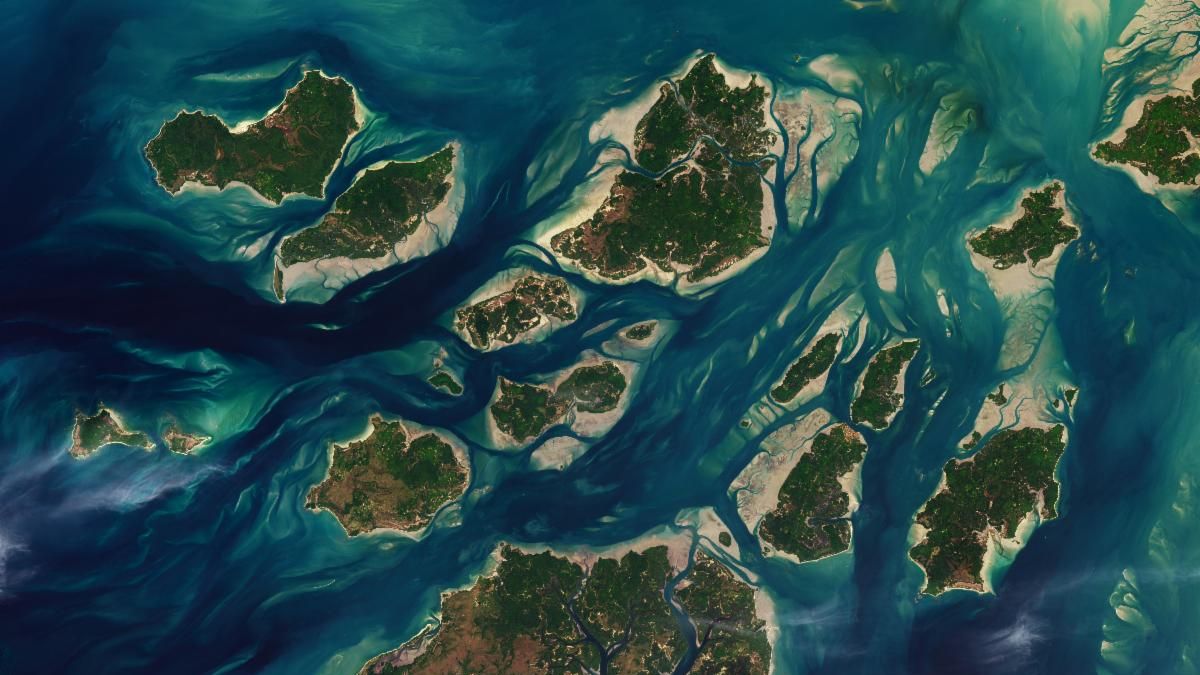 A satellite image shows a cluster of green islands surrounded by beige sand flats and networks of channels full of dark blue water.