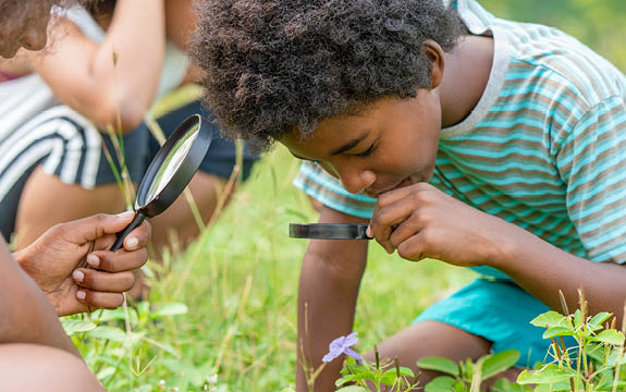 Photo of a child looking at a plant through a magnifying glass. 