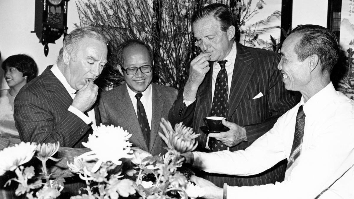 Gov. Hugh L. Carey tries Chinese sweets with Fung Tung (Assistant Director of Housing) and Sir Murray MacLehose in 1981
