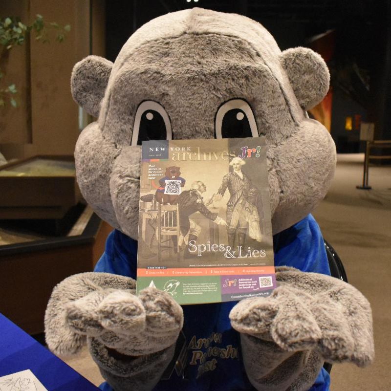 Archie the Jr! Archivist beaver holds up a copy of "Archives Jr!" magazine insert.