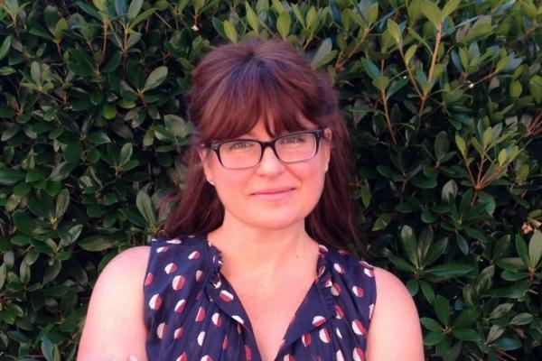 woman with dark auburn hair and glasses smiles at camera