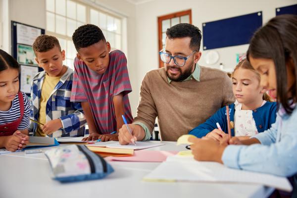 male teacher sitting at table with students in classroom