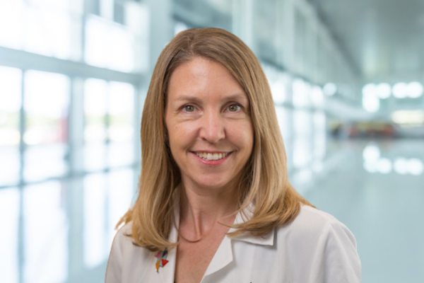 blonde woman wearing lab coat stands in bright hallway