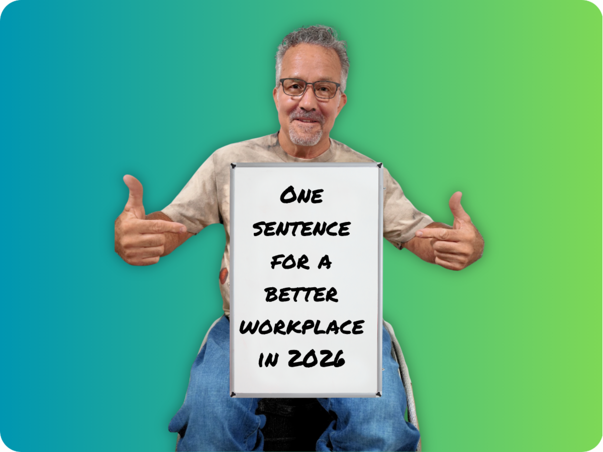 Andy in his chair with a sign on his lap that reads "One sentence for a better workplace in 2026".