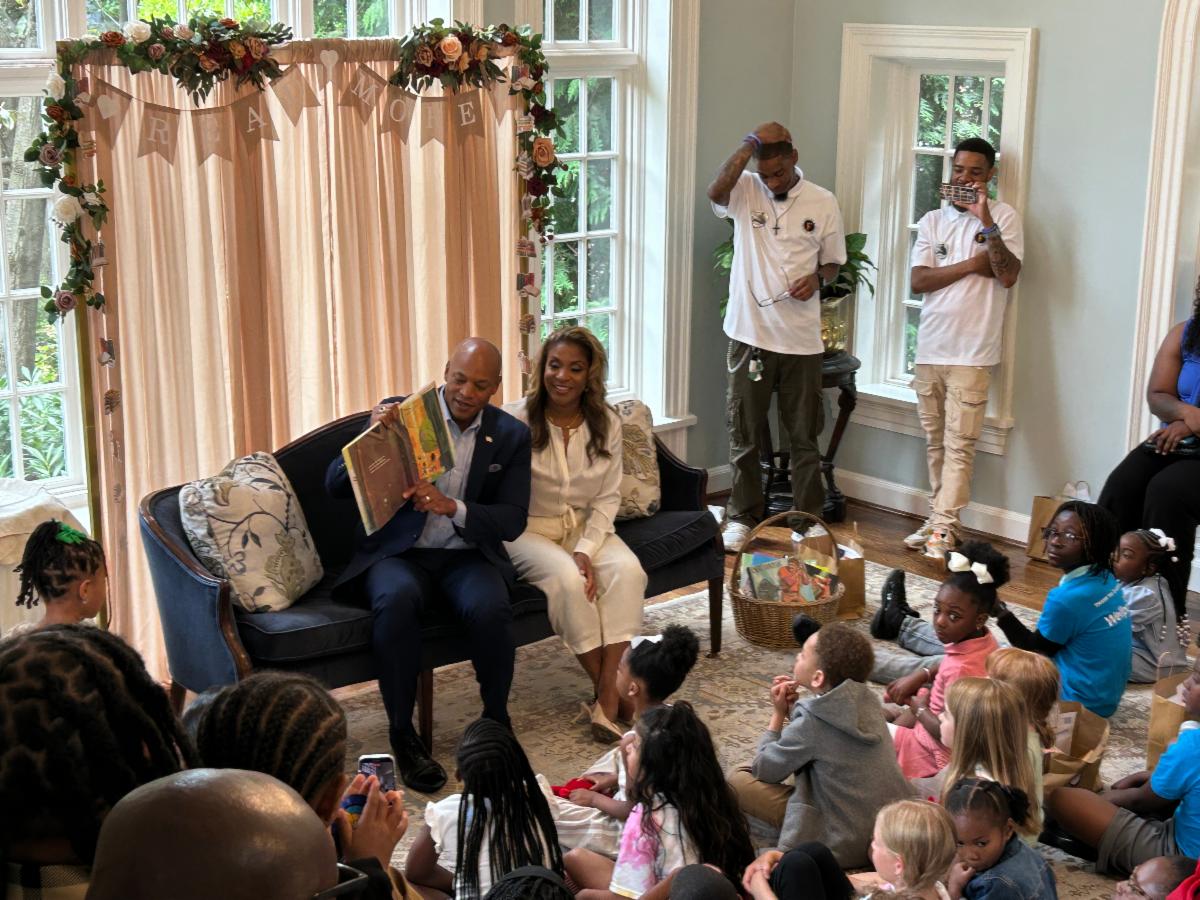 Governor Wes Moore reads a story to a room of children as First Lady Dawn Moore sits beside him.