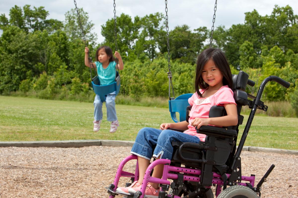 Little girl in a wheelchair sits in front of swings.