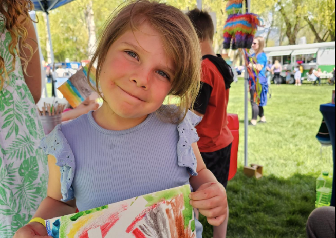 A girl holds up artwork at an outdoor fair