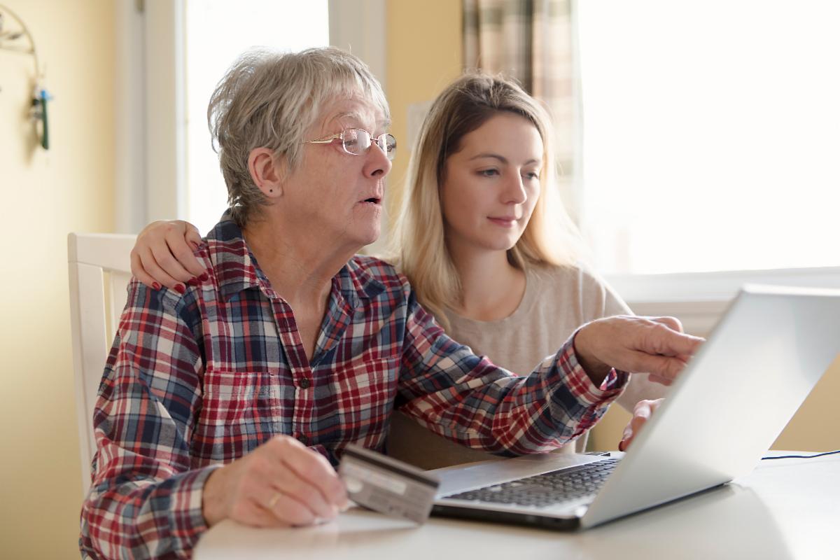 An older woman pointing at a computer screen, sitting with a younger woman who appears to be helping her.