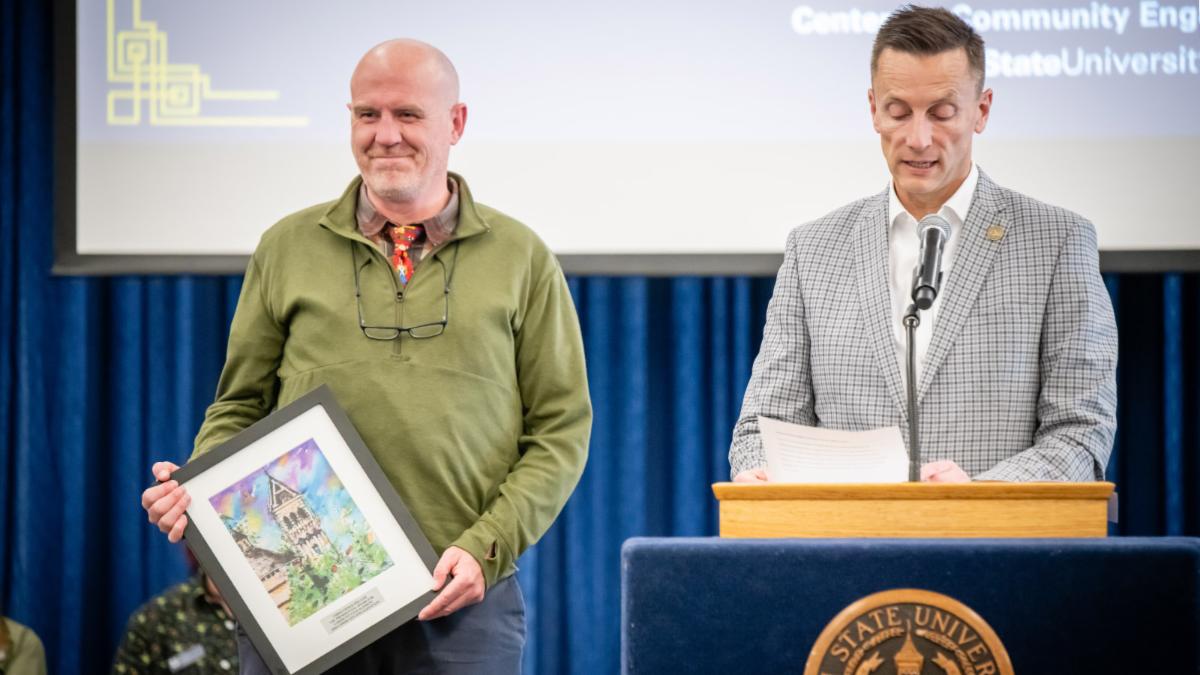Christopher holds his award next to USU President Brad Mortensen