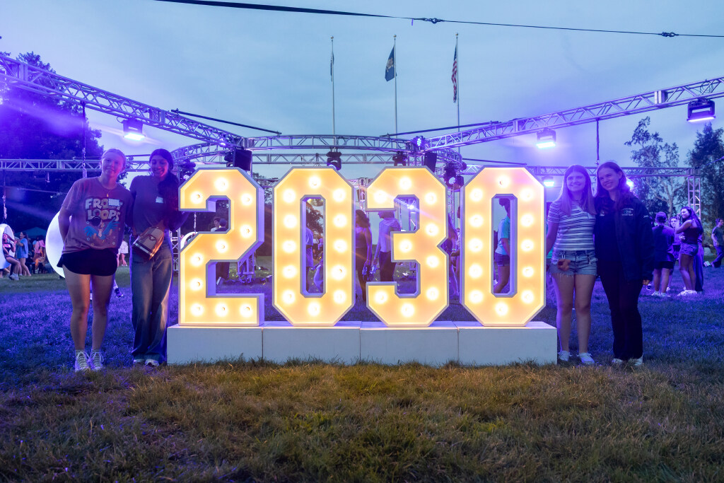 UConn students enjoy the fire pits and glow swings on the Founders Green on Thursday, Aug. 27, 2026. (Sydney Herdle/UConn Photo).  They are standing in front of a sign that says 2030. 