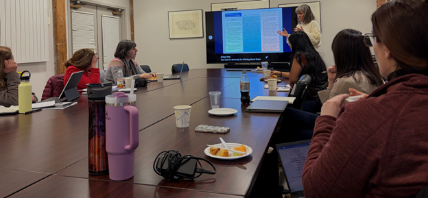 Picture of a woman talking to people sitting on a rectangular table