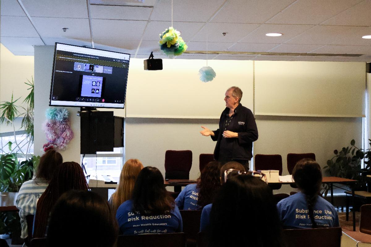 Picture of a speaker looking at a screen and an audience looking at him.