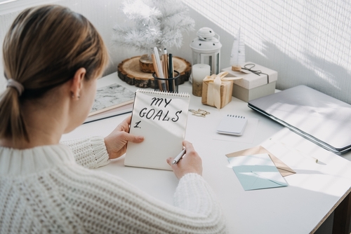 New year resolution_ New goals_ Start new year_ planning and setting goals for the next year. Woman in white sweater writing handwritten text My Goals in open notepad on the table.