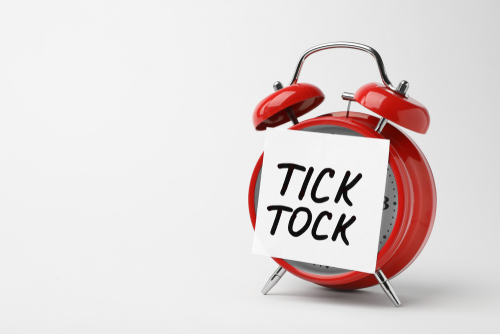 Alarm clock and sticky note with words TICK TOCK on white background. Time concept