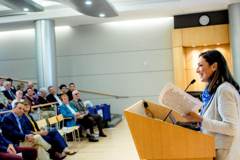 A woman at the podium on the right addressing an auditorium of people