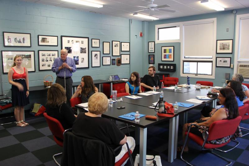 A group of volunteers sitting at a confereance room table watching a training demonstration with a man and a woman standing in front of group