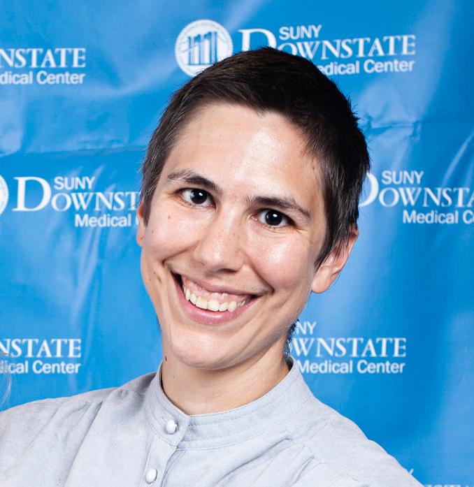 A person with short dark hair wearing a white button shirt smiles against a blue background