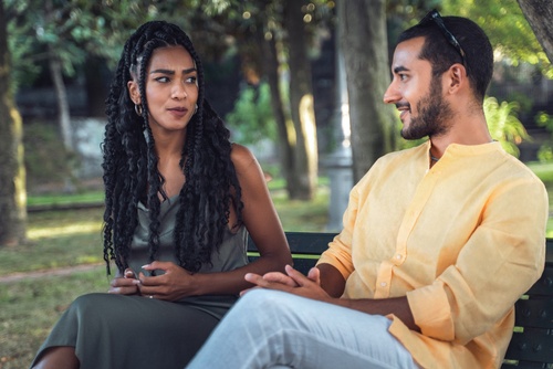 Adult man and woman talking together in a park while sitting on a bench. Calm outdoor conversation_ reflection_ communication_ and interpersonal relationship concepts.