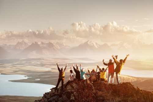 Big group of people having fun in success pose with raised arms on mountain top against sunset lakes and mountains. Travel_ adventure or expedition concept