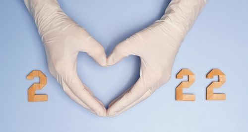 2022 New year resolution healthy life during Covid 19 pandemic concept. Hand of a doctor in medical glove gesture in heart shape between number 2022 on blue background. Vaccine_ Vaccinated_ Support