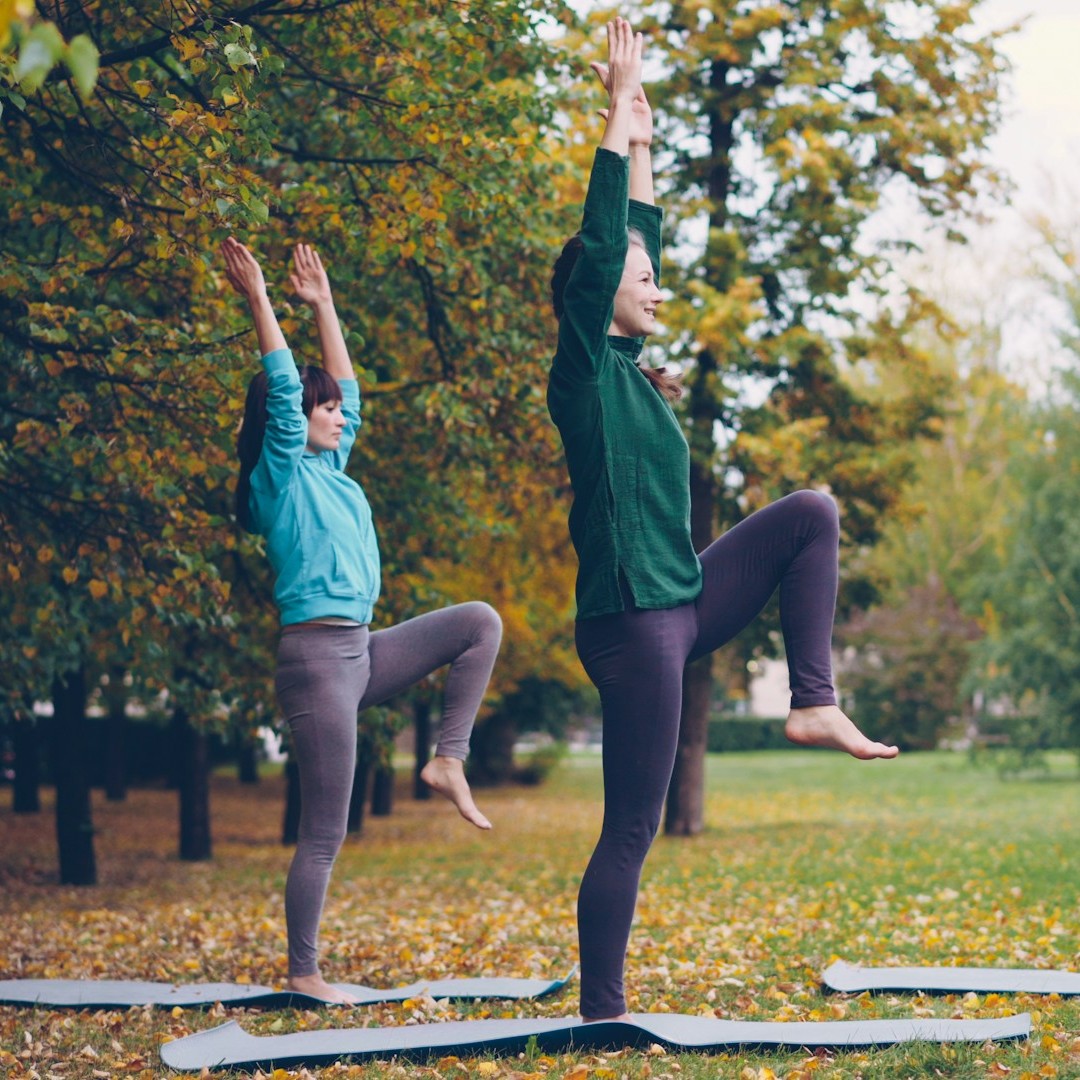 Two people stand outside on yoga mats, reaching for the sky