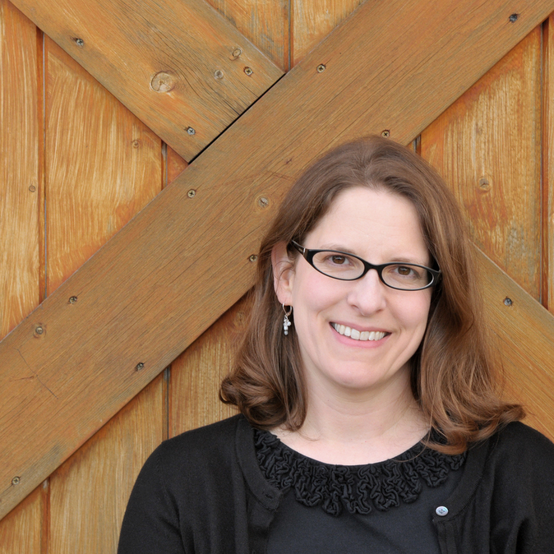 Photo of presenter, Kathy MacMillan, in a black top and black glasses against a brown, wooden door.