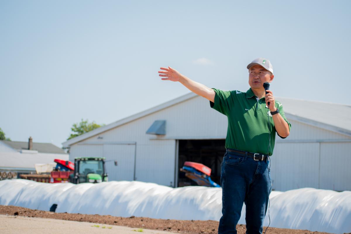 Wei Liao standing infant of a barn talking into a microphone 