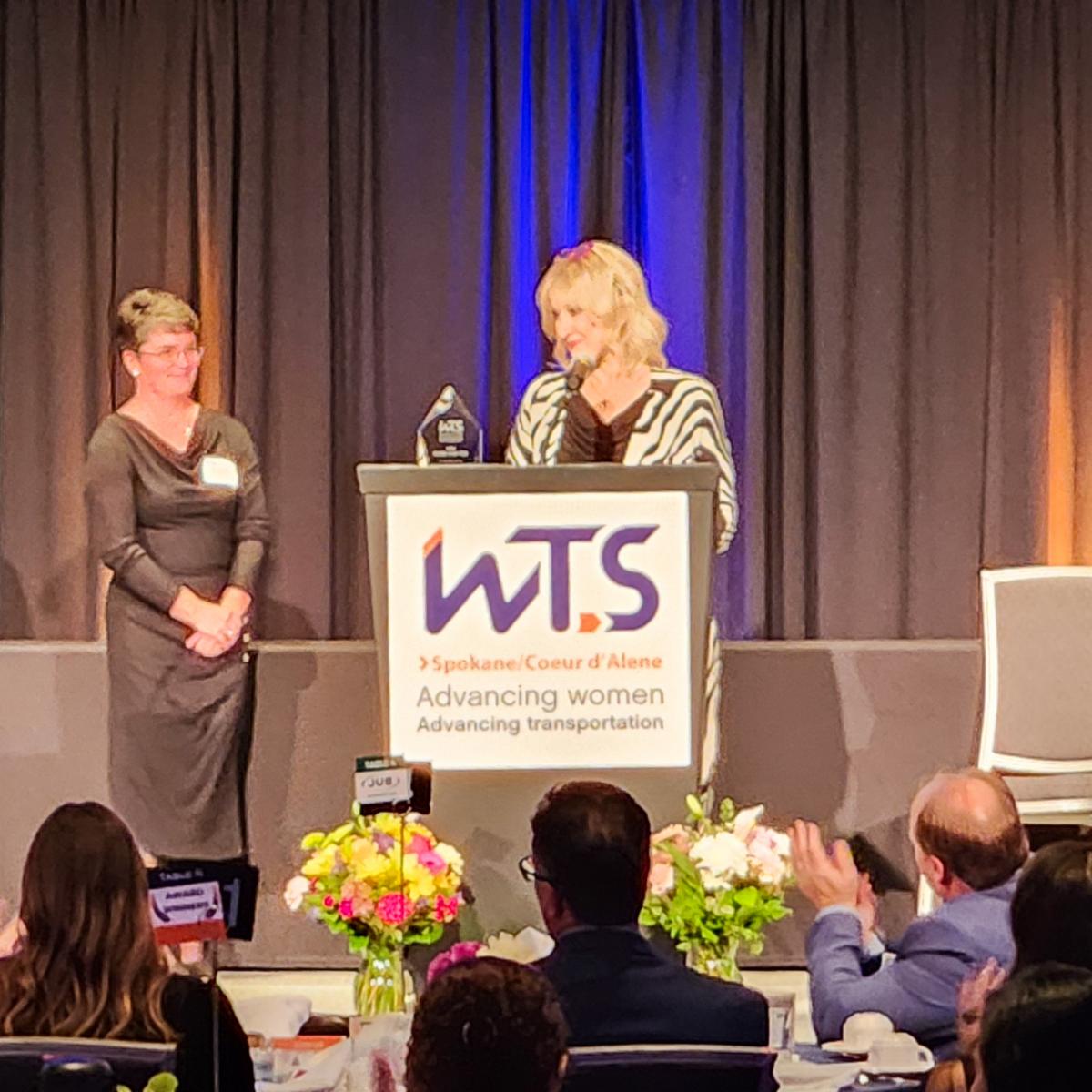A photo of E. Susan Meyer at a podium accepting her Woman of the Year WTS award.