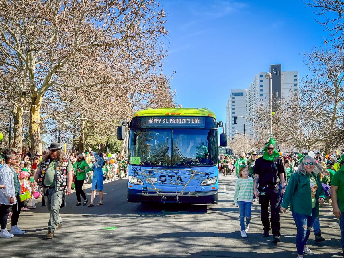 A photo of an STA bus driving in the St. Patrick’s Day Parade with a large crowd