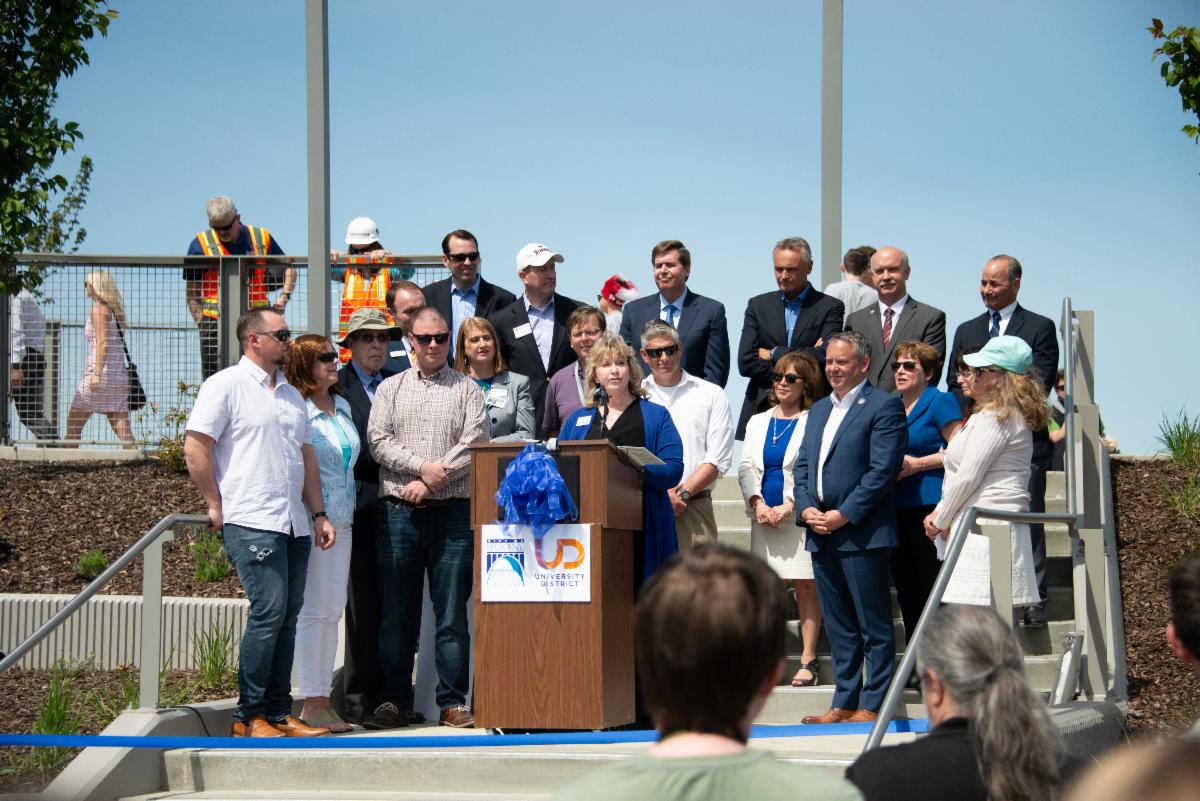 A photo of Susan speaking on stage at a ribbon cutting event